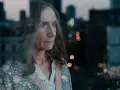Małgorzata Hajewska patrzy przez okno na nocne miasto. W tle widać światła i budynki.
