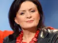 Zofia Czernicka w czarnej skórzanej kurtce i wyrazistej czerwonej biżuterii, siedząca na pomarańczowej kanapie.