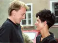 Olimpia Burczyk i mężczyzna w czarnej bluzie śmieją się do siebie, stojąc na tle budynku z oknami.