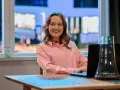 Uśmiechnięta Dorota Krempa pracuje przy laptopie, siedząc przy stole. W tle widać okno z nocnym widokiem.