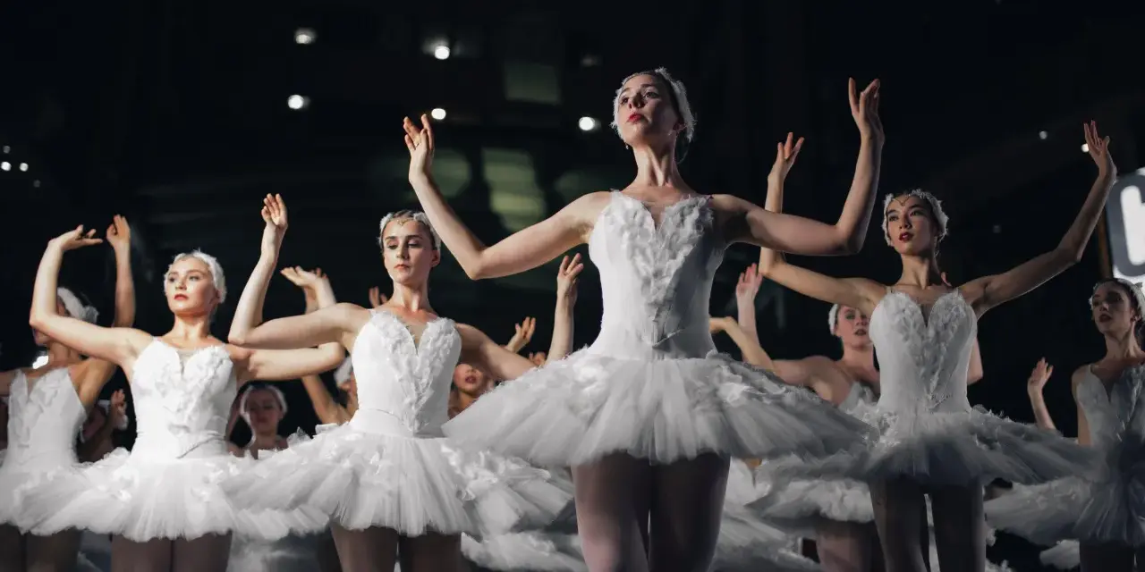 Tancerki w białych tutu, jak żywe cytaty o tańcu, unoszą ramiona w harmonijnym ruchu.