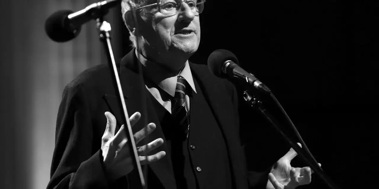 Starszy mężczyzna w okularach, Jan Matyjaszkiewicz, przemawia do mikrofonu.