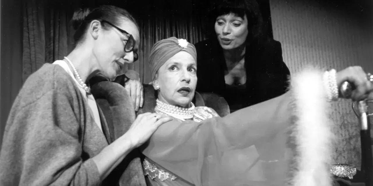 Marlena Milwiw młoda, w otoczeniu dwóch kobiet, w teatralnej scenie.