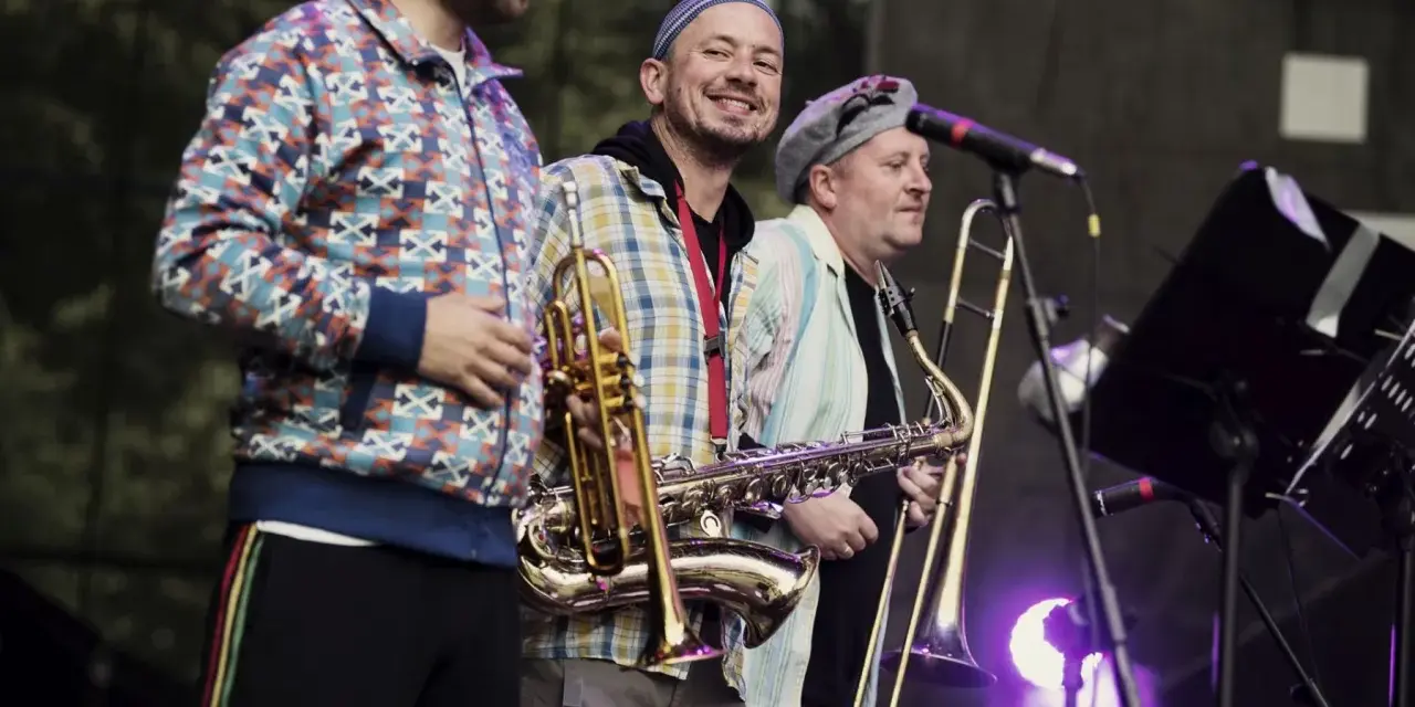 Adam Kłosiński z zespołem na scenie, grają na saksofonie i puzonie.