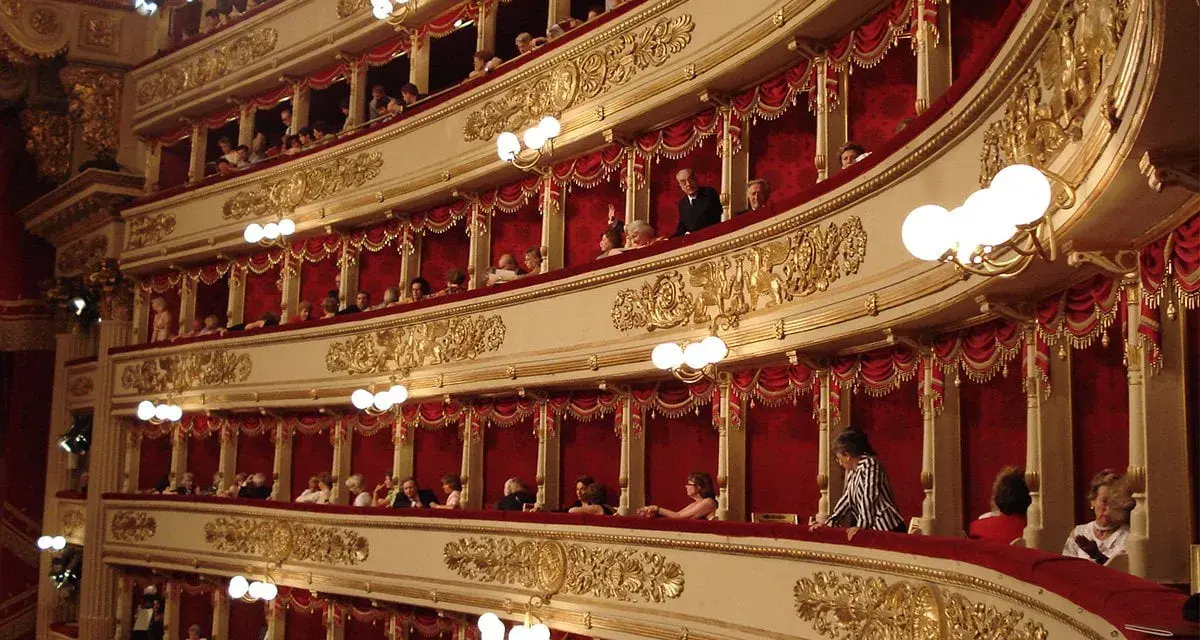 Wnętrze teatru La Scala, z widownią w lożach ozdobionych złotem i czerwonymi zasłonami.