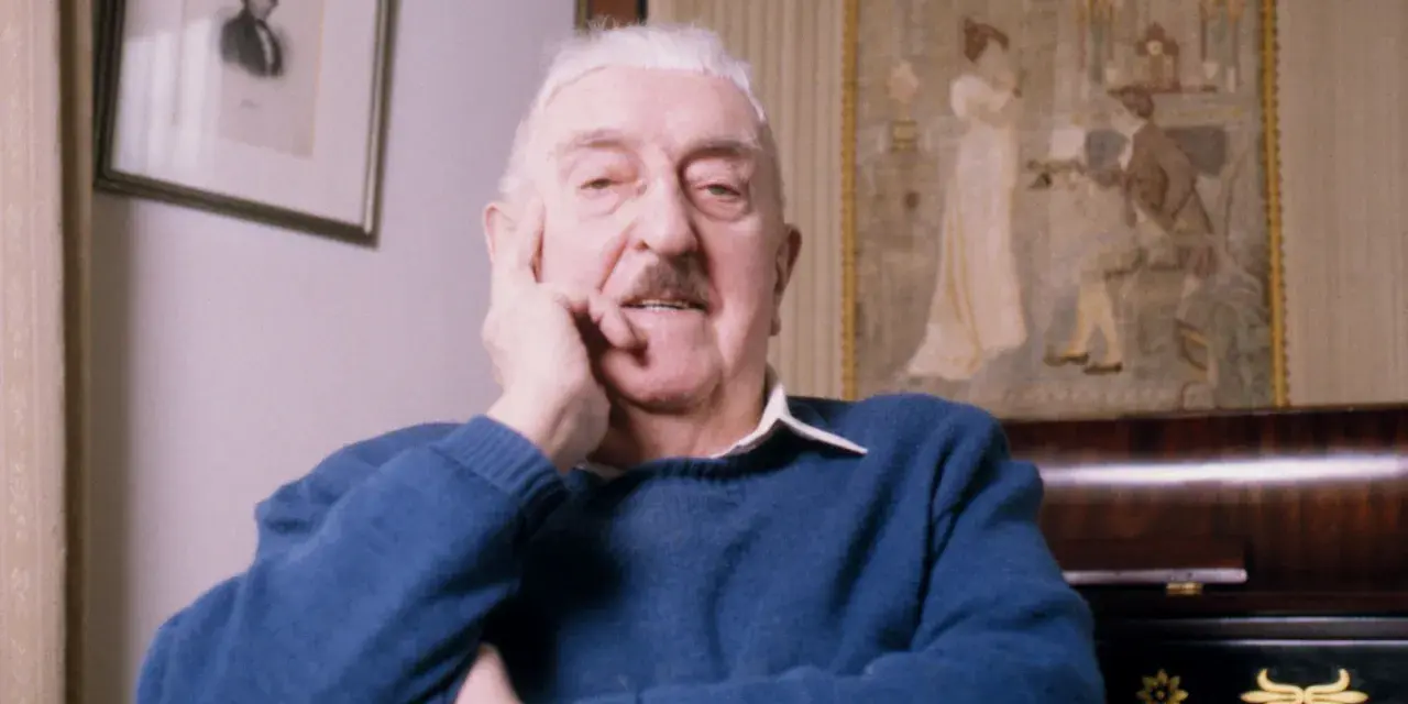 Jerzy Waldorff, znany z zamiłowania do kultury i sztuki, w niebieskim swetrze. Jego wykształcenie i pasje widoczne w tle.