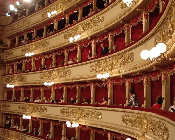 Wnętrze teatru La Scala, z widownią w lożach ozdobionych złotem i czerwonymi zasłonami.