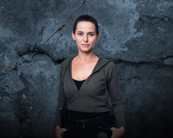 Natalia Brudniak w wojskowym stylu, z rękami w kieszeniach, na tle zniszczonej ściany.