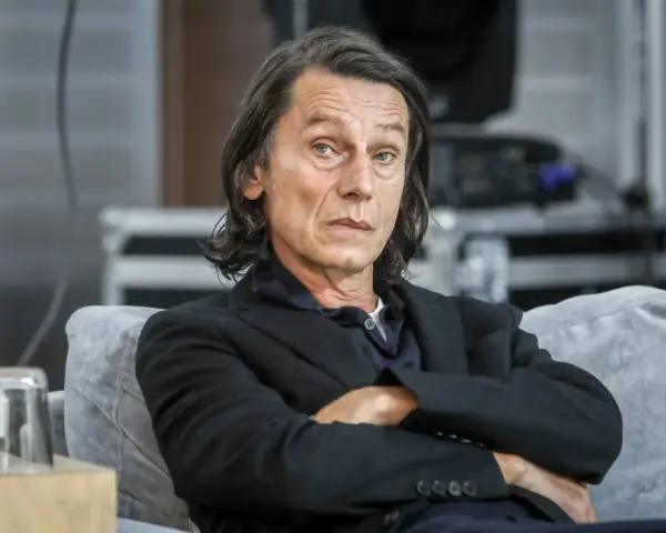 Krzysztof Warlikowski, reżyser teatralny, w czarnym garniturze, siedzi na kanapie. Jego życie prywatne budzi zainteresowanie.