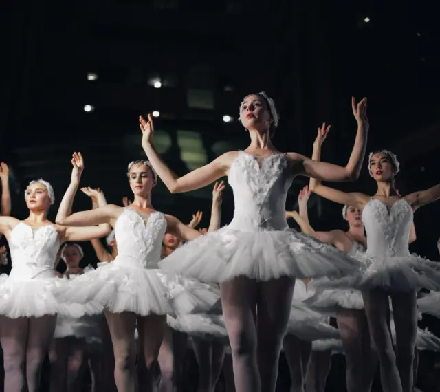 Tancerki w białych tutu, jak żywe cytaty o tańcu, unoszą ramiona w harmonijnym ruchu.