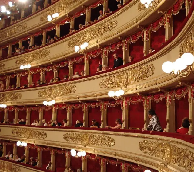 Wnętrze teatru La Scala, z widownią w lożach ozdobionych złotem i czerwonymi zasłonami.