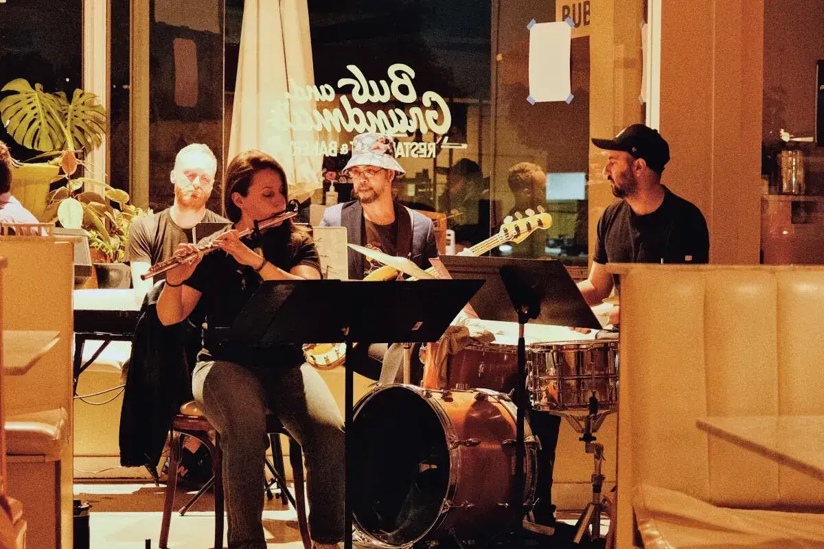 Muzyk grający do kotleta, czyli zespół jazzowy w restauracji. Kobieta gra na flecie, obok basista i perkusista.