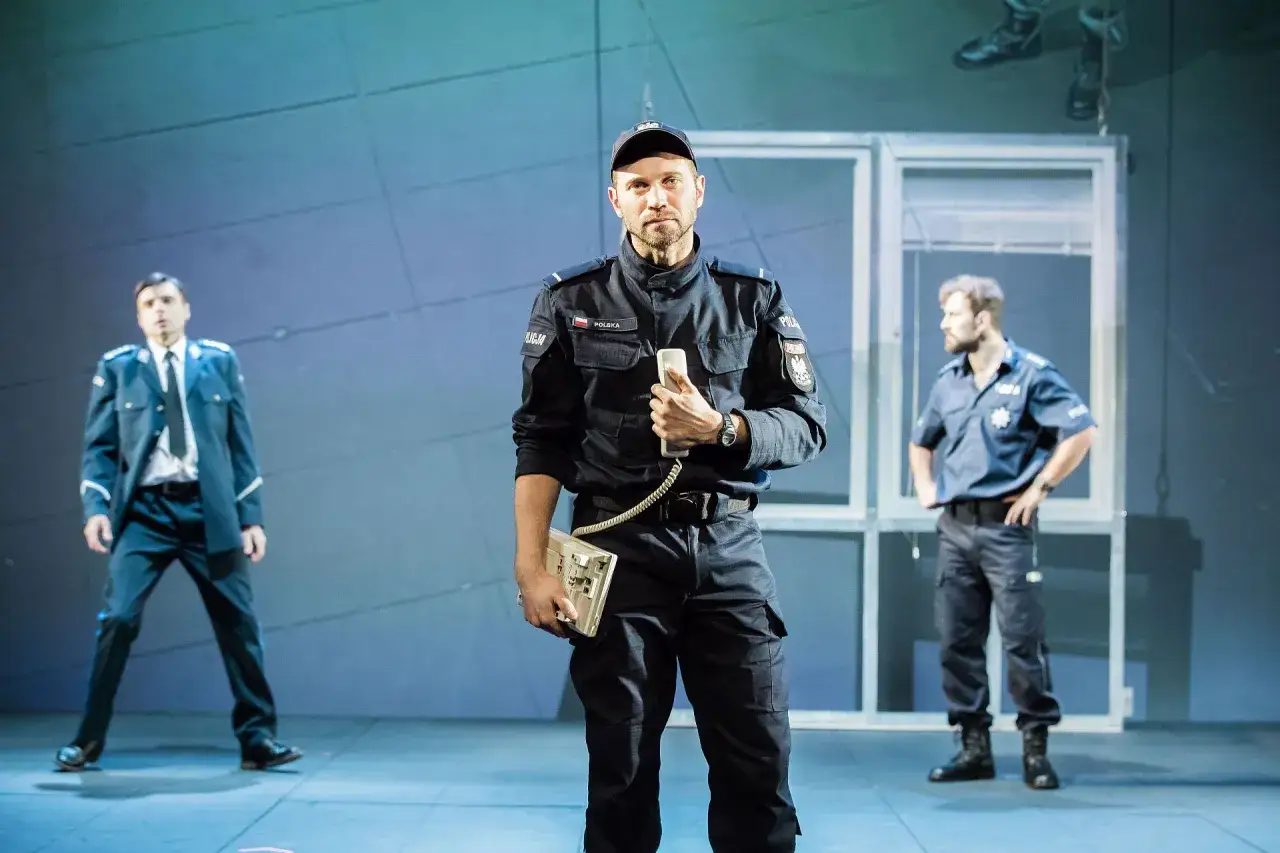 Arkadiusz Brykalski w mundurze policjanta trzyma telefon. Obok niego dwaj inni funkcjonariusze.