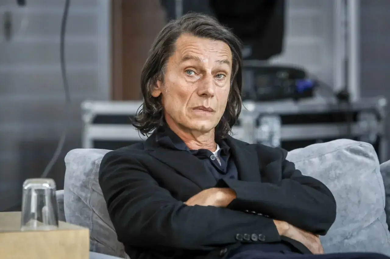 Krzysztof Warlikowski, reżyser teatralny, w czarnym garniturze, siedzi z założonymi rękami. Jego życie prywatne budzi zainteresowanie.