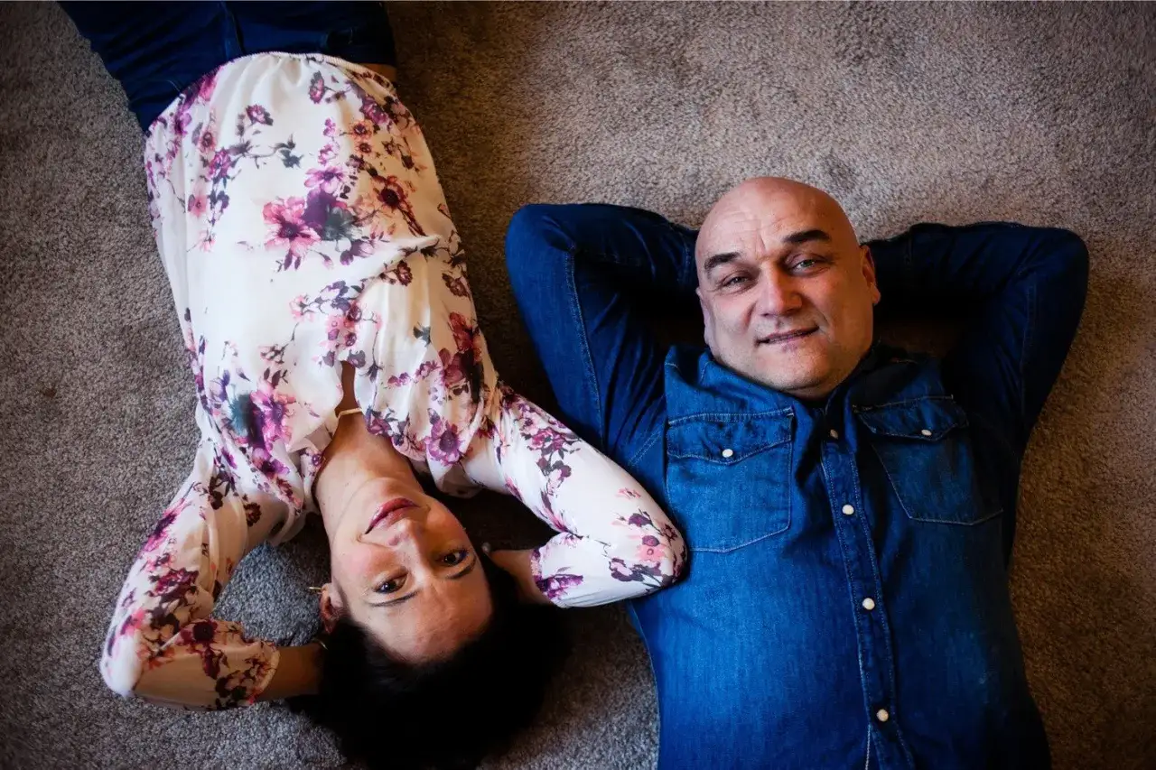 Marta Bizoń z mężem, leżą na dywanie. Ona w kwiecistej bluzce, on w dżinsowej koszuli.