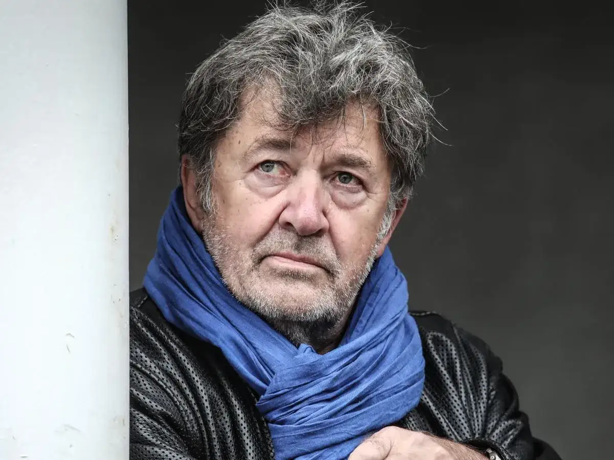 Olek Krupa, z siwymi włosami i niebieskim szalem, spogląda zamyślony.