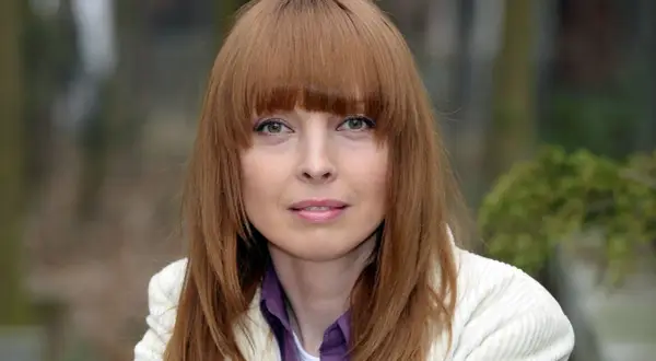 Katarzyna Tlałka w białej marynarce, z rudymi włosami i grzywką. Czyżby myślała o swoich mężach?