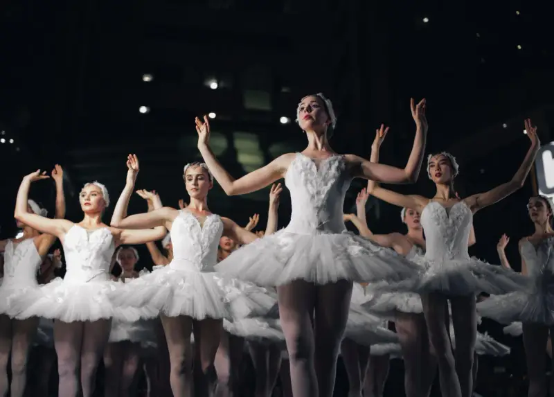 Tancerki w białych tutu, jak żywe cytaty o tańcu, unoszą ramiona w harmonijnym ruchu.