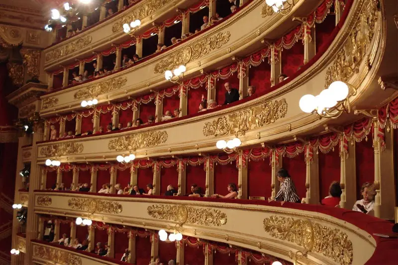 Wnętrze teatru La Scala, z widownią w lożach ozdobionych złotem i czerwonymi zasłonami.
