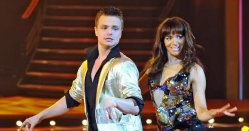 Tomasz Schejbal, kim jest? Tancerz w złotym stroju i jego partnerka w błyszczącej sukience na scenie.